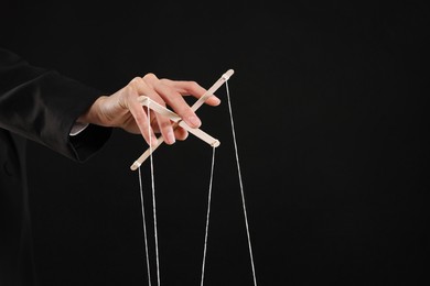 Photo of Woman pulling strings of puppet on black background, closeup. Space for text