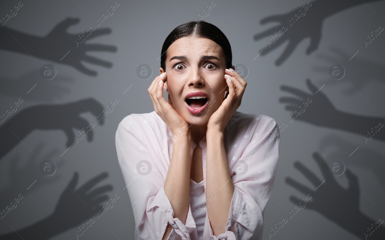 Image of Paranoid delusion. Scared woman screaming on grey background. Shadows of hands reaching for her symbolizing fear and anxiety