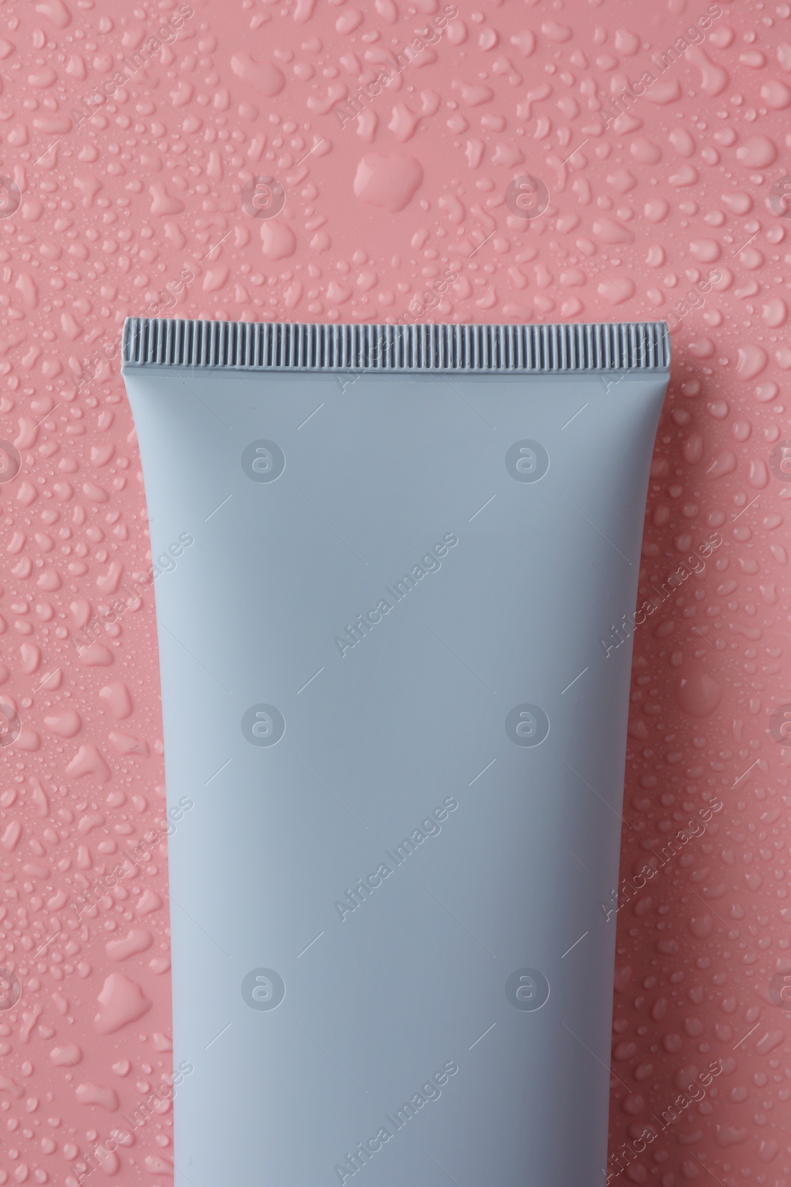 Photo of Moisturizing cream in tube on pink background with water drops, top view