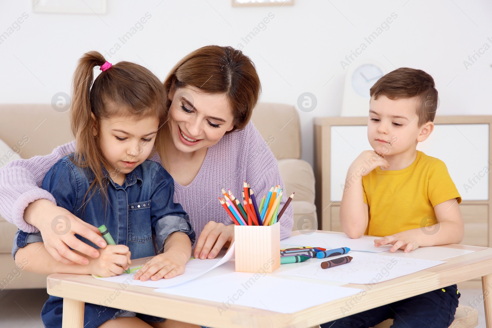 Photo of Cute little children and their nanny drawing at home