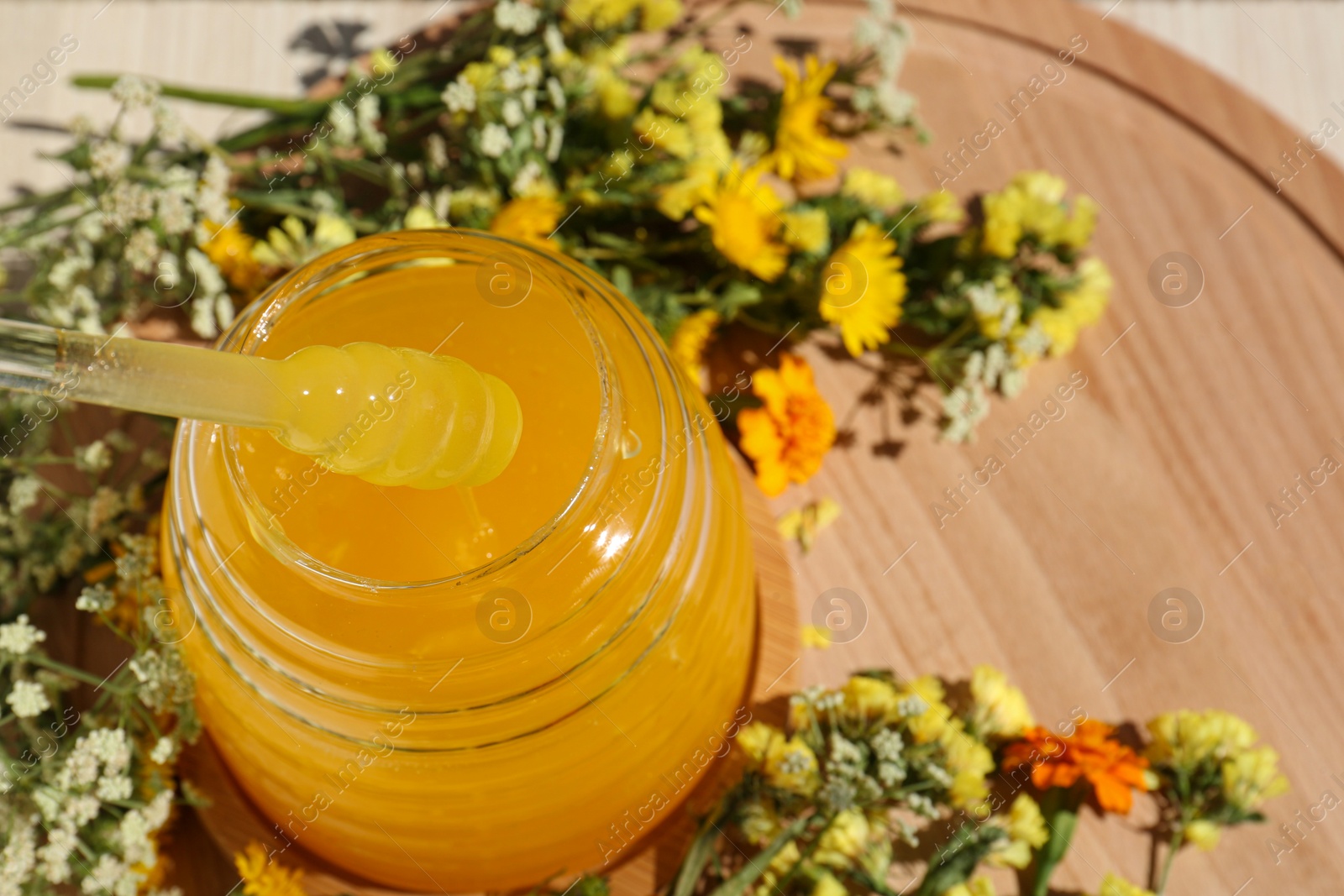 Photo of Taking delicious fresh honey with dipper from glass on wooden table