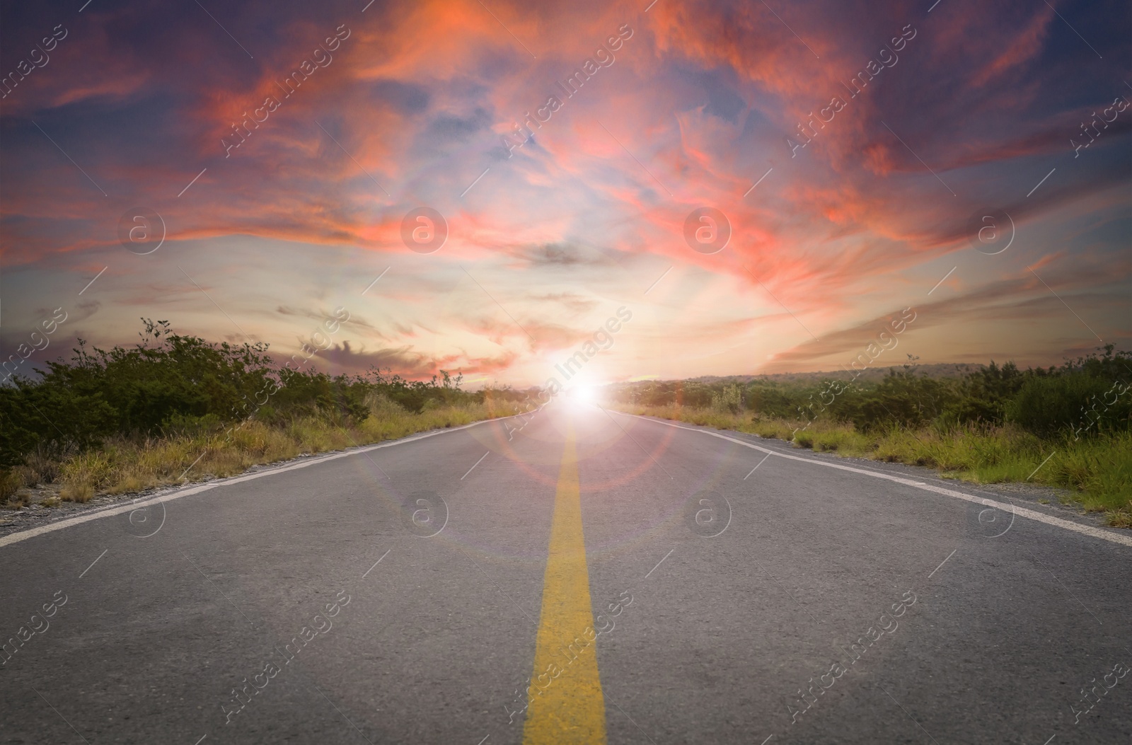 Image of Empty asphalt road through field at sunset