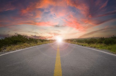 Empty asphalt road through field at sunset