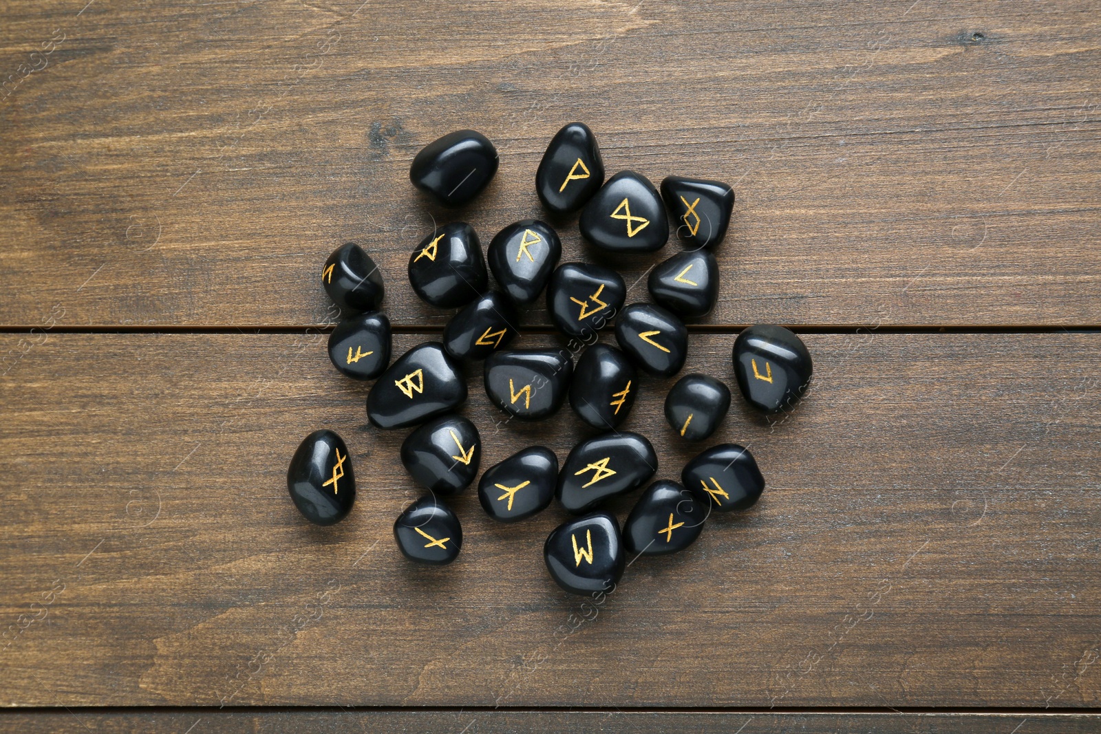 Photo of Pile of black rune stones on wooden table, flat lay