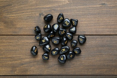 Pile of black rune stones on wooden table, flat lay