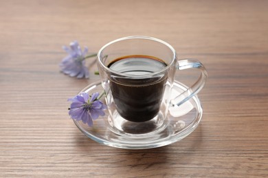 Photo of Glass cup of delicious chicory drink and flowers on wooden table