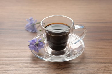 Glass cup of delicious chicory drink and flowers on wooden table