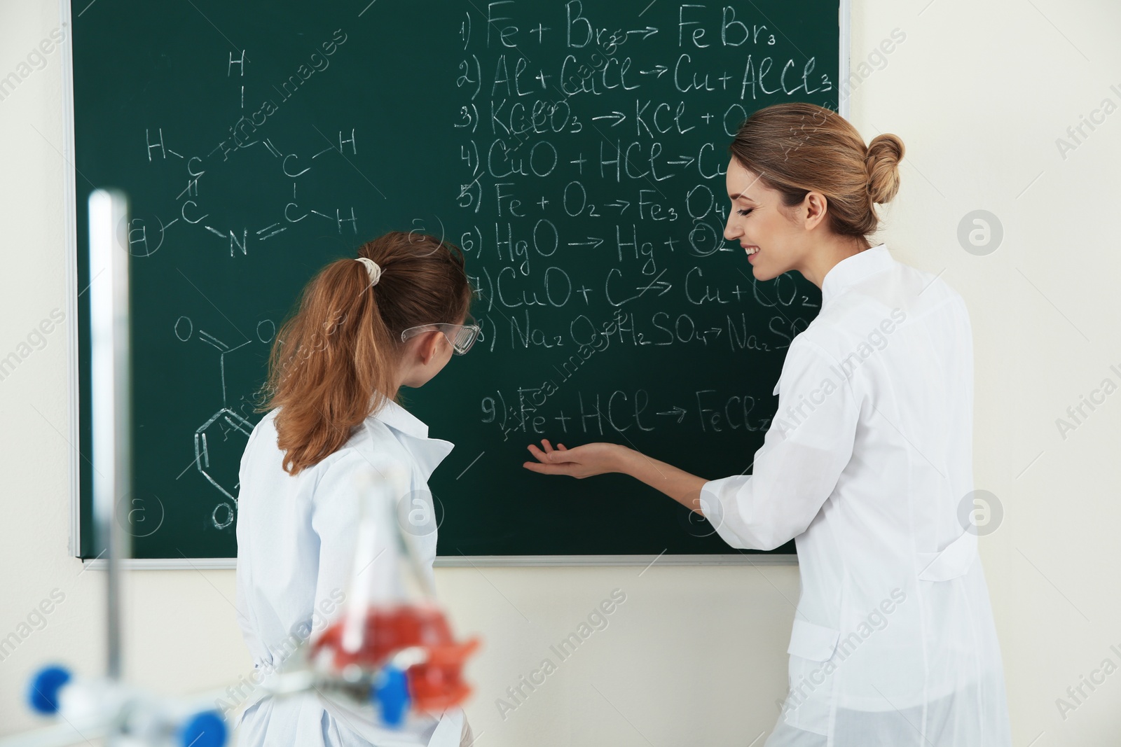 Photo of Teacher with pupil at blackboard in chemistry class