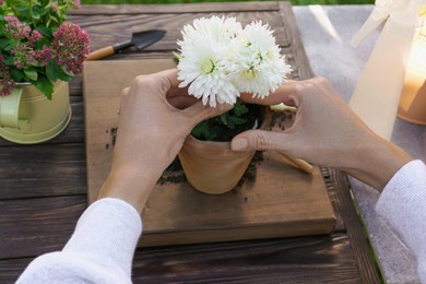 Photo of Woman planting flower into pot at wooden table, closeup. Gardening work