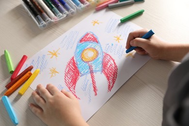 Little boy drawing rocket with soft pastel at wooden table, closeup. Child`s art