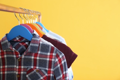 Rack with stylish children clothes on yellow background, closeup. Space for text