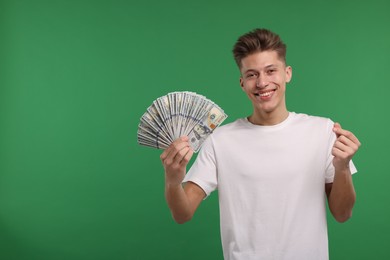 Photo of Happy man with dollar banknotes showing money gesture on green background. Space for text