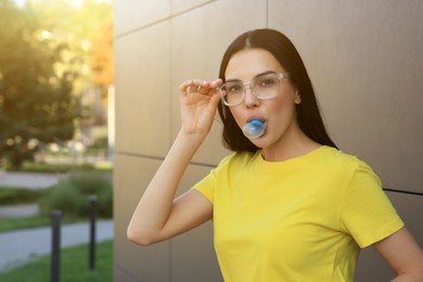 Beautiful woman blowing gum near dark tiled wall outdoors, space for text