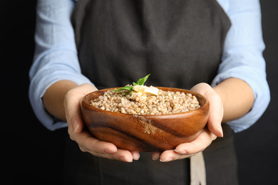 Photo of Woman holding bowl with tasty buckwheat porridge on black background, closeup
