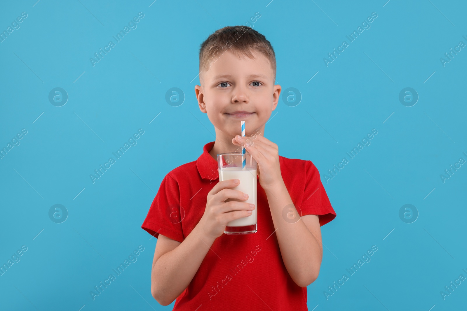 Photo of Cute boy with glass of fresh milk on light blue background