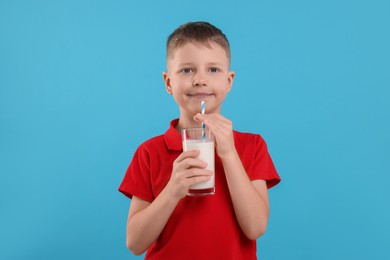 Cute boy with glass of fresh milk on light blue background