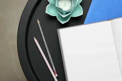Photo of Notebooks, pencils and decorative holder with candle on round table indoors, top view. Closeup
