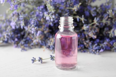 Bottle of essential oil and lavender flowers on white wooden table