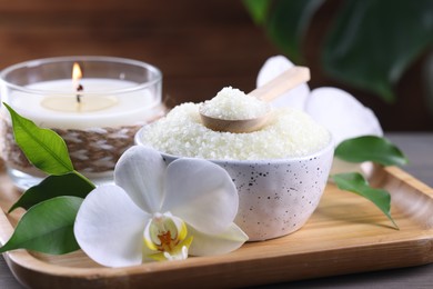 Photo of Natural sea salt in bowl, candle and beautiful orchid flower on wooden table, closeup