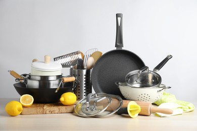Photo of Set of clean kitchenware and lemons on wooden table against light background