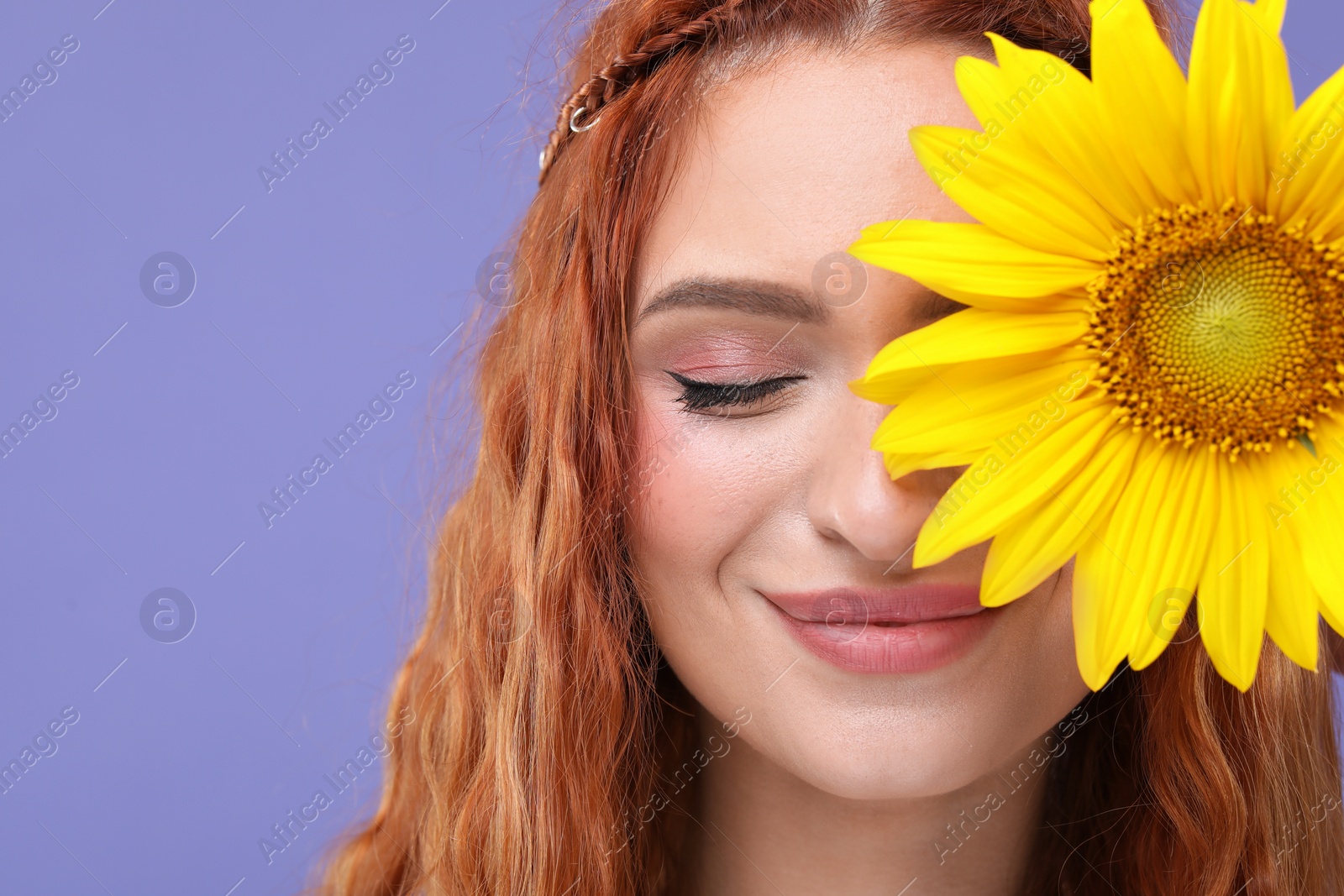 Photo of Beautiful young hippie woman covering eye with sunflower on violet background, closeup