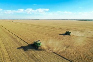 Beautiful aerial view of modern combine harvesters working in field on sunny day. Agriculture industry