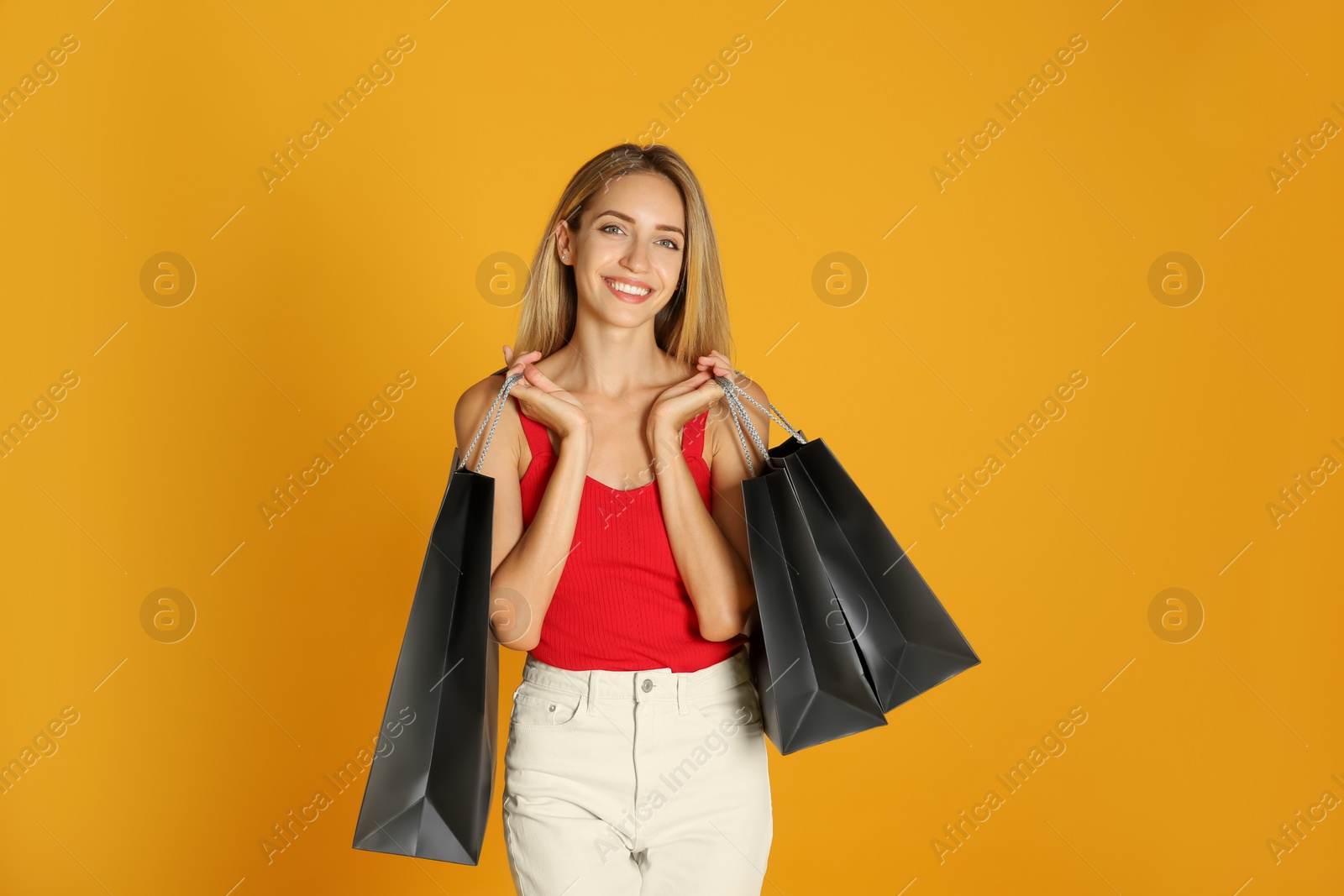 Photo of Happy young woman with shopping bags on yellow background. Black Friday Sale