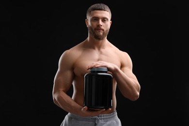 Photo of Young man with muscular body holding jar of protein powder on black background