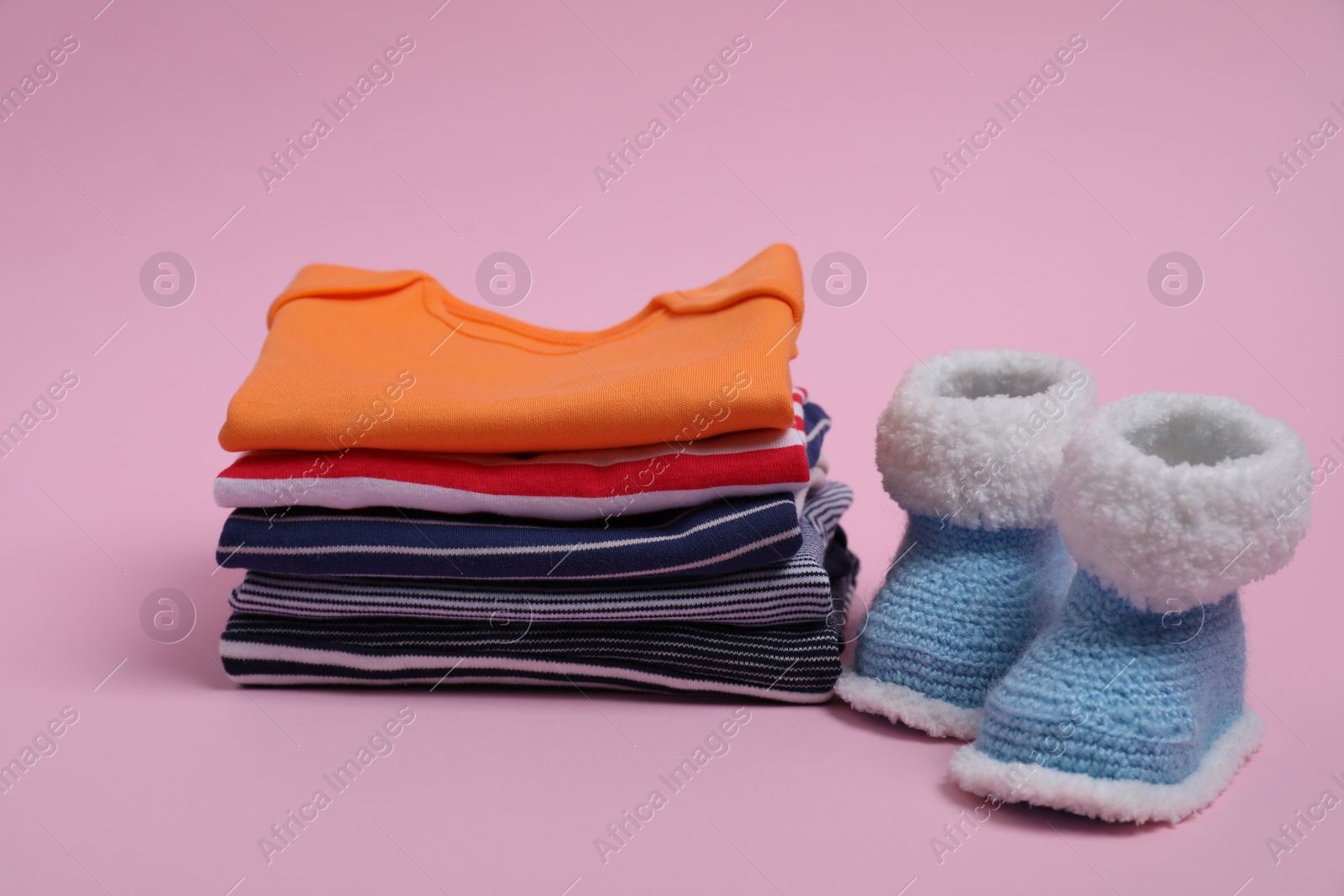 Photo of Stack of clean baby clothes and small booties on pink background