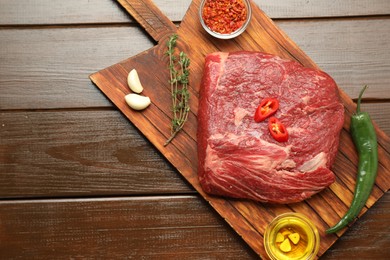 Photo of Fresh raw beef cut, spices and oil on wooden table, top view. Space for text