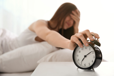 Young woman turning off alarm clock at home in morning, focus on hand