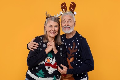 Photo of Senior couple in Christmas sweaters and reindeer headbands on orange background