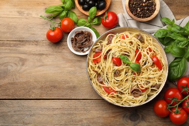 Photo of Delicious pasta with anchovies, tomatoes and spices on wooden table, flat lay. Space for text