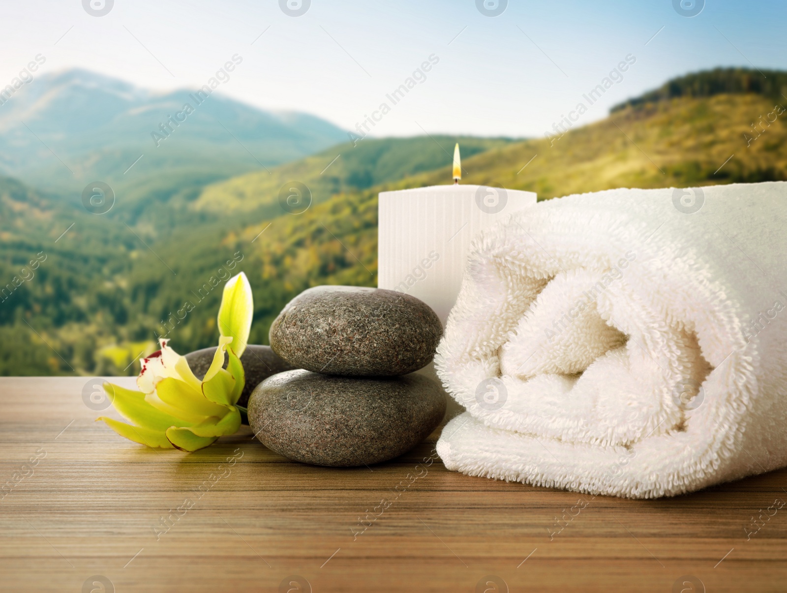 Image of Fresh towel, spa stones and exotic flower on wooden table against beautiful mountain landscape
