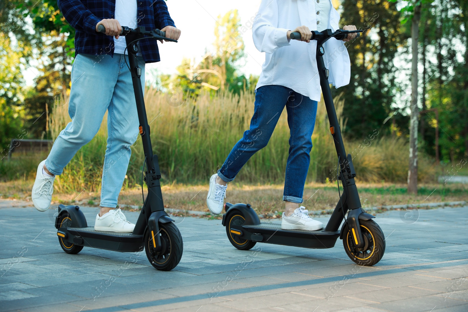 Photo of Couple riding modern electric kick scooters in park, closeup