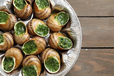 Photo of Delicious cooked snails on wooden table, top view. Space for text