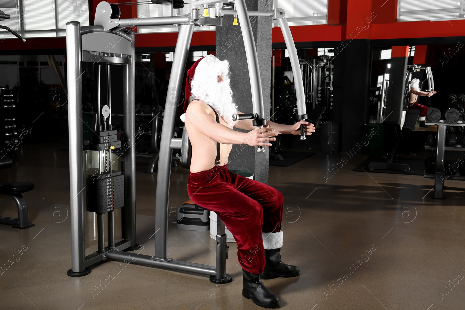 Photo of Young shirtless Santa Claus training in modern gym