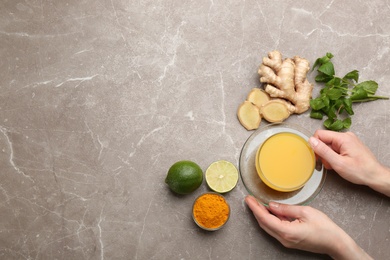 Photo of Woman holding cup of immunity boosting drink at table with ingredients, top view. Space for text