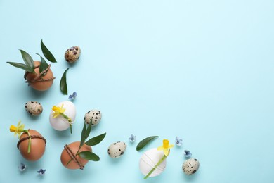Photo of Easter eggs decorated with green leaves and flowers on light blue background, flat lay. Space for text
