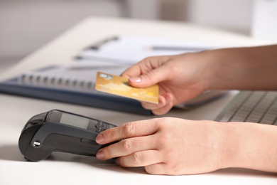 Photo of Woman using modern payment terminal at table indoors, closeup