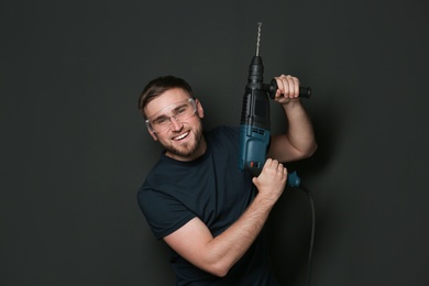 Photo of Young working man with rotary hammer on dark background