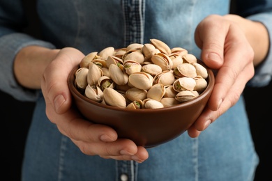 Woman holding bowl with pistachio nuts on black background, closeup