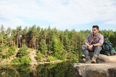 Young man on rock near lake and forest. Camping season