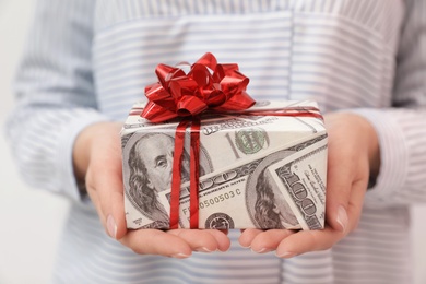 Woman holding gift box wrapped in dollars, closeup