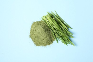 Pile of wheat grass powder and fresh sprouts on light blue table, flat lay