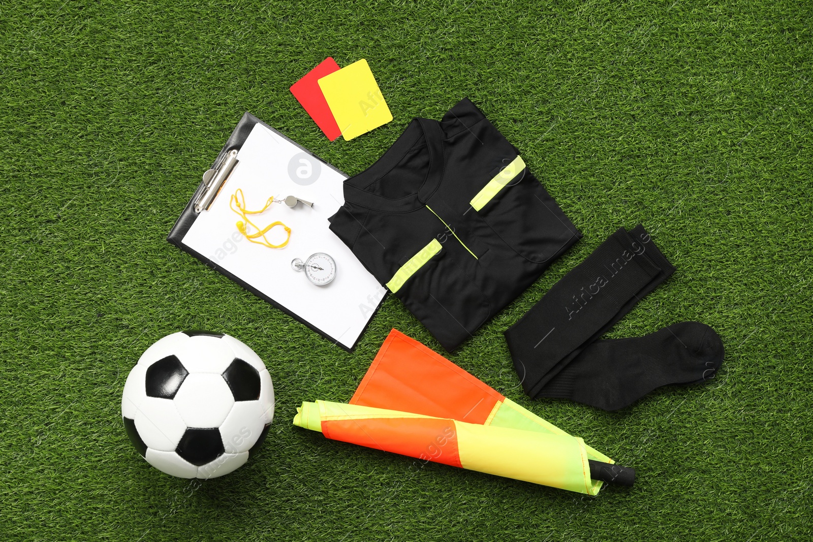 Photo of Uniform, soccer ball and other referee equipment on green grass, flat lay