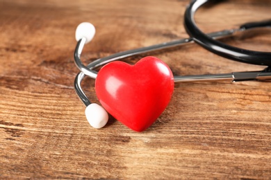 Photo of Stethoscope and small red heart on wooden table. Heart attack concept