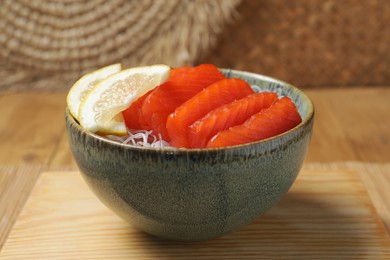 Photo of Delicious salmon sashimi served with funchosa and lemon on wooden table, closeup