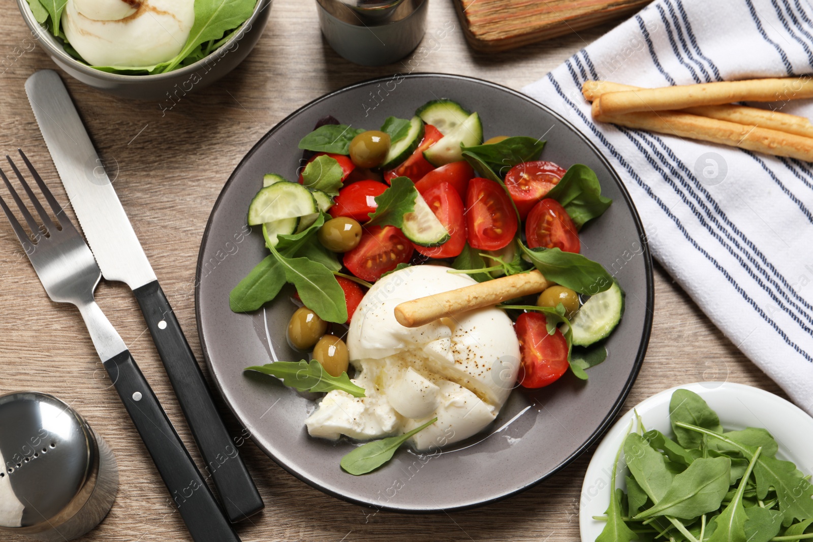 Photo of Delicious burrata salad served on wooden table, flat lay