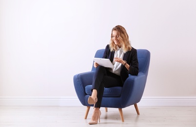 Young woman with tablet sitting in armchair indoors